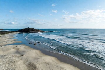 A serene coastal landscape featuring sandy beaches, crashing waves, and a distant rocky outcrop under a clear sky
