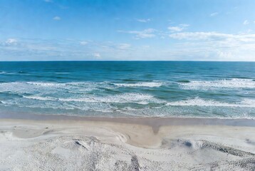 Serene coastal landscape: aerial view of a sandy beach meeting the vast blue ocean with gentle waves