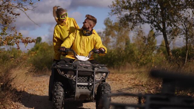 Two riders on quad in autumn preparing helmets and sharing laugh, sunlit scrubland, friendly shoulder pat, readying for off road route, goggles and jackets