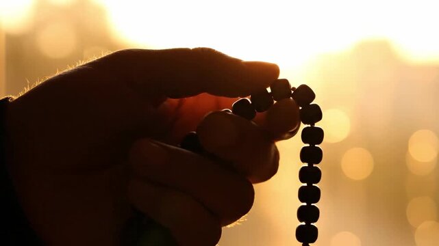 Silhouette Close-up of Hand Counting Prayer Beads at Sunset