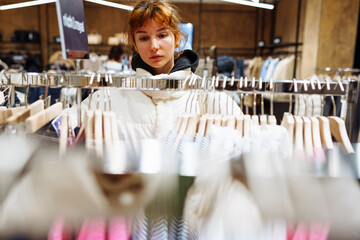 young attractive red-haired woman choosing clothes in boutique