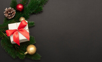 White gift box with twine, pine branches, frosted cone and gold ornaments on dark background, festive and elegant