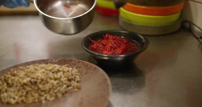 Ladling food. Portioned dish. Chef pouring hot red liquid meal in black bowls. Hand serving borsch on restaurant kitchen interior table.