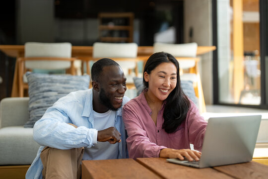 Happy young diverse, multiethnic couple planning budget, reading good news on laptop at home - Powered by Adobe