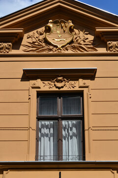 An ornate window on a historical orange facade is crowned by a golden relief featuring the coat of arms of the Triune Kingdom of Croatia, Slavonia, and Dalmatia