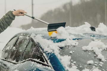 Cleaning Snow from a Car Hood with a Brush After Winter Snowfall