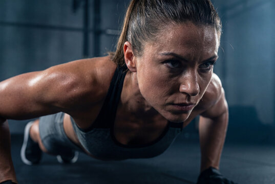 Fit athletic woman doing push-ups in gym, sweat on face