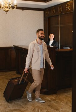 Man smiling arriving at hotel checking in with suitcase