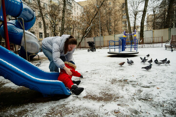 Parent assists bundled-up child on a snowy playground slide. Urban winter setting with playground...