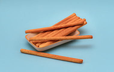 This professionally lit studio advertisement features an overflowing cluster of crispy snack sticks piled high on a small plate against a clean blue background. Great for digital marketing.