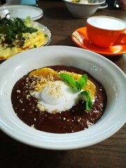 Delicious dessert bowl featuring creamy chocolate pudding topped with orange slices, whipped cream, and crushed nuts, served in a cozy cafe setting with a vibrant cup of coffee