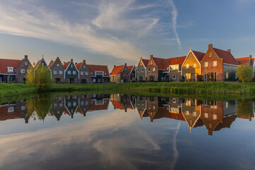Fototapeta premium A row of traditional Dutch houses in historic Volendam with steep gables and orange tiles. The facades reflect in the calm water at the bank during golden light.