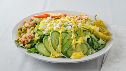 Fresh salad topped with sliced cucumbers, tomatoes, feta cheese, and drizzled with yellow dressing.