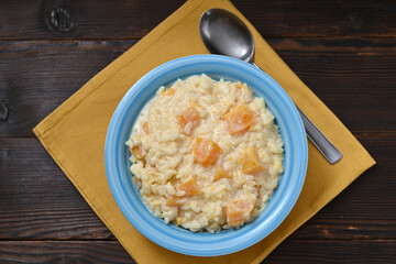 Pumpkin rice porridge in a bowl on a wooden table, flat lay