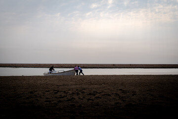 Three Local Men Cooperatively Pushing Traditional Fishing Boat from Vast Sandy Riverbank into the Calm Waters of Shatt Al-A