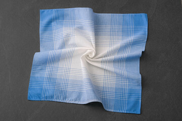 A white and light blue plaid handkerchief is folded into a swirl pattern and placed on a dark gray surface.