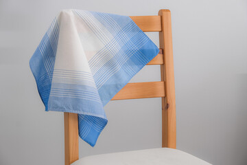 A classic blue and white patterned cotton handkerchief is draped over the backrest of a simple wooden chair against a plain gray background.