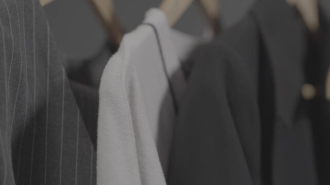 Close up view of stylish jackets and sweaters hanging on a rack in a clothing store. The camera pans across different fashionable garments on wooden hangers.

