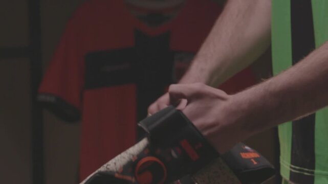 Close-up of an African American football player pulling up orange socks over his knees. The athlete is getting dressed and preparing for a soccer match in the locker room.

