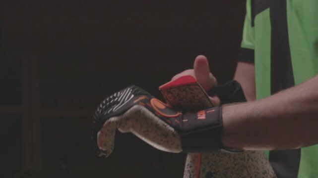 Close-up of an African American football player pulling up orange socks over his knees. The athlete is getting dressed and preparing for a soccer match in the locker room.

