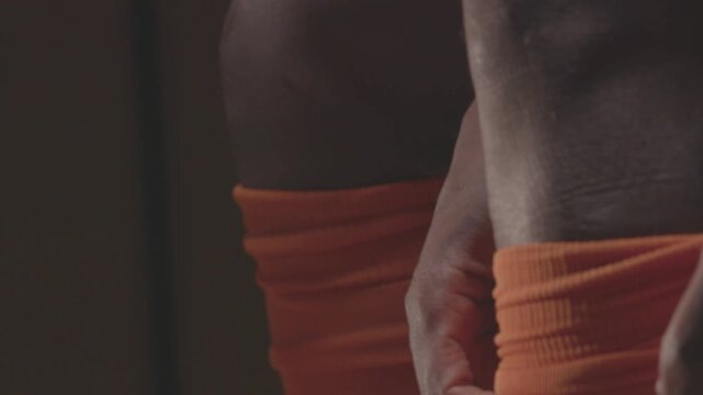 Close-up of an African American football player pulling up orange socks over his knees. The athlete is getting dressed and preparing for a soccer match in the locker room.

