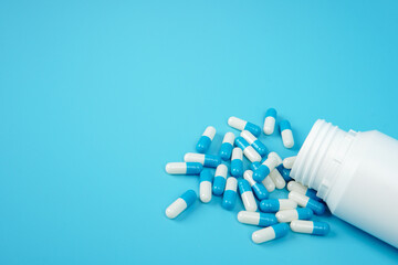 Blue and white medicine capsules spilled from bottle representing pharmaceutical supply, healthcare treatment, medication management, and medical industry concept with clean copy space.