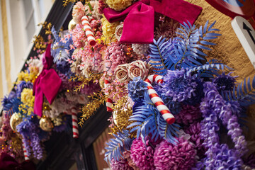 Vibrant Christmas garland with candy canes, pink roses, and blue ferns decorating a sweet shop facade in the historic city of Bruges, Belgium.