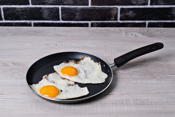 Cooking eggs in a skillet on a kitchen countertop with a stone wall background