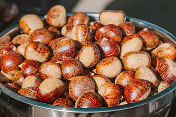 Freshly roasted chestnuts in a metal bowl and on a grill, warming up as a popular autumn and winter snack