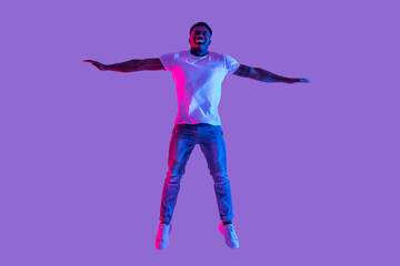 A young black man leaps in the air, surrounded by vibrant neon lights. He expresses happiness and excitement, celebrating a personal victory. His dynamic pose captures pure joy and energy.