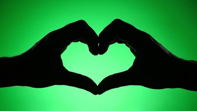 Silhouette of hands forming a heart shape gesture on green screen background