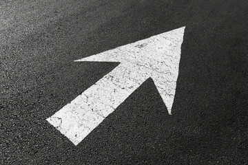 White directional arrow painted on asphalt road surface. Forward direction traffic marking on dark pavement. Urban street navigation symbol. Minimal transportation concept background. Guidance sign.