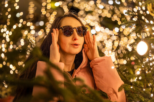 A surprised girl wearing sunglasses at a Christmas market in Europe. In the background, bokeh from the lights, with reflections of the market lights in her sunglasses.