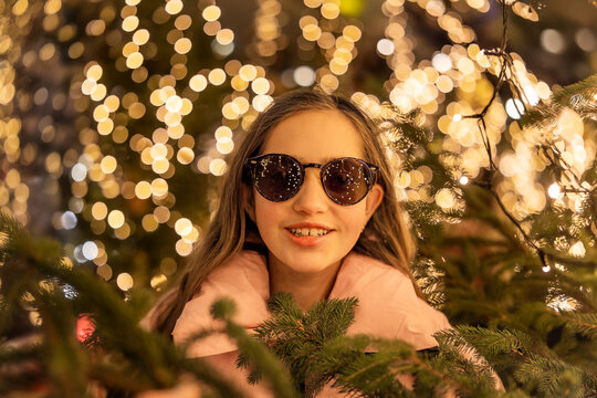 A surprised young teenage girl wearing sunglasses at a Christmas market in Europe. In the background, bokeh from the lights, with reflections of the market lights in her sunglasses.