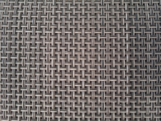 Close-up of woven gray and beige flat PVC plastic rattan or wicker texture. Synthetic material, flat weave, interlocking geometric pattern background, outdoor patio furniture, durable fibers, textile.
