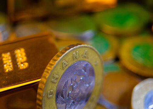 A high-detail shot of bimetallic 1 and 2 Ghana cedi coins featuring the national Coat of Arms, paired with polished gold bars on a dark surface, symbolizing Ghana's financial assets and mineral wealth