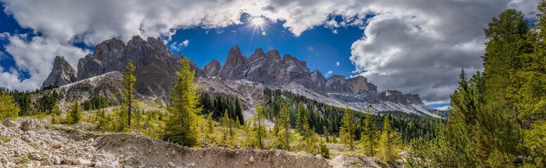 Fototapeta premium Panoramic Dolomites mountain landscape with jagged limestone peaks, alpine meadows, rocky ridges, dramatic geology, Italian Alps scenery, high altitude terrain, clear sky, natural environment