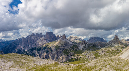 Panoramic Dolomites mountain landscape with jagged limestone peaks, alpine meadows, rocky ridges, dramatic geology, Italian Alps scenery, high altitude terrain, clear sky, natural environment