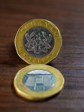 Two 10-sided 2 Cedi coins from Ghana. The upright coin shows the National Coat of Arms; the flat one displays Jubilee House. Both feature a bi-metallic design with a brass ring and nickel center