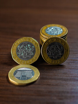 A collection of Ghanaian cedi coins, including bi-metallic 1 and 2 cedi pieces. They feature national symbols like the Jubilee House, Scales of Justice, and Coat of Arms on gold and silver surfaces.