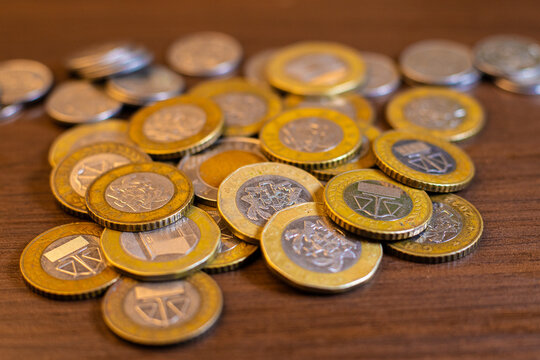 A heap of bimetallic Ghanaian Cedi coins rests on a wooden surface. The shot highlights the gold and silver tones of the 1 and 2 Cedi denominations, showing details of the Scales of Justice symbol.