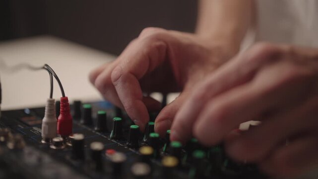 Creating sound, male hand adjusting dials and faders on dj mixer console, mixing audio for music production, live performance or recording, close-up. Shooting in slow motion.