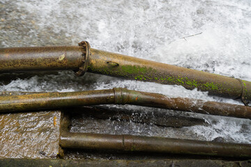 Close Up Of A Rusted Metal Pipe With Moss Covered Branches Partially Submerged In Moving Water