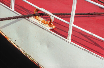 Detail of a rusty cleat and coiled rope on a boat’s weathered red deck showing signs of aging