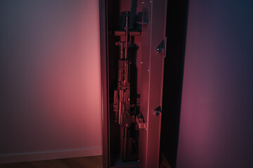 Modern assault rifle securely stored in a narrow, tall gun safe, illuminated by dramatic red and...