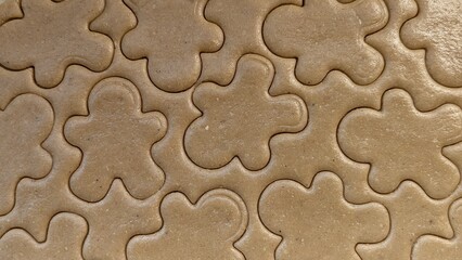 Overhead flat lay view of raw gingerbread cookie dough texture with multiple gingerbread man shapes cut out, creating a repeating pattern for holiday baking concepts.