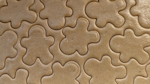 Overhead flat lay view of raw gingerbread cookie dough texture with multiple gingerbread man shapes cut out, creating a repeating pattern for holiday baking concepts.