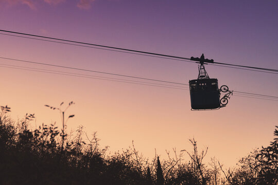 Cable car transporting a bicycle against a vibrant purple and orange sunset sky, creating a striking silhouette. Concept of active travel - Powered by Adobe