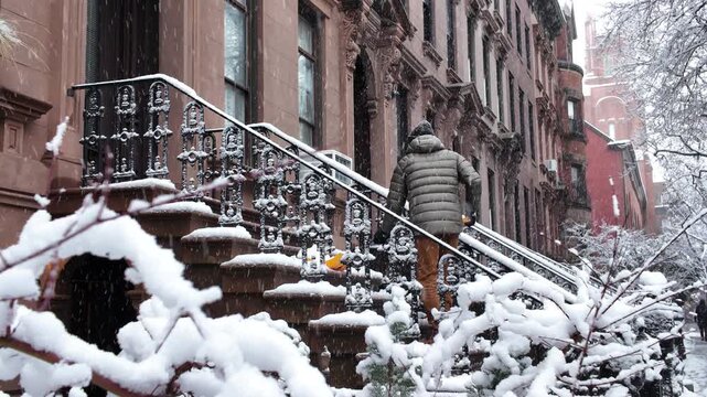 tighter shot of man shoveling snow on stoop in front of Brooklyn brownstones