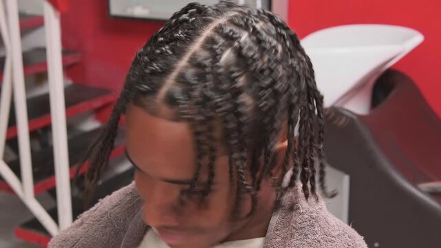 Smiling teen boy showing finished afro braids, touching his hair proudly in barbershop front-view shot